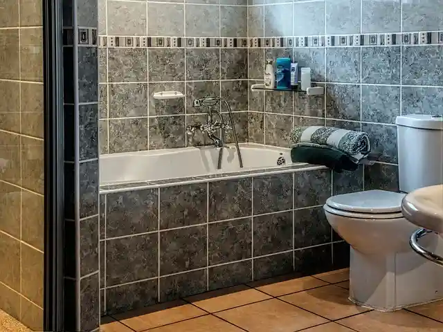 A bathroom with a white bathtub, toilet, and sink. The floor and shower walls are lined with small gray tiles that have a slightly textured, three-dimensional appearance